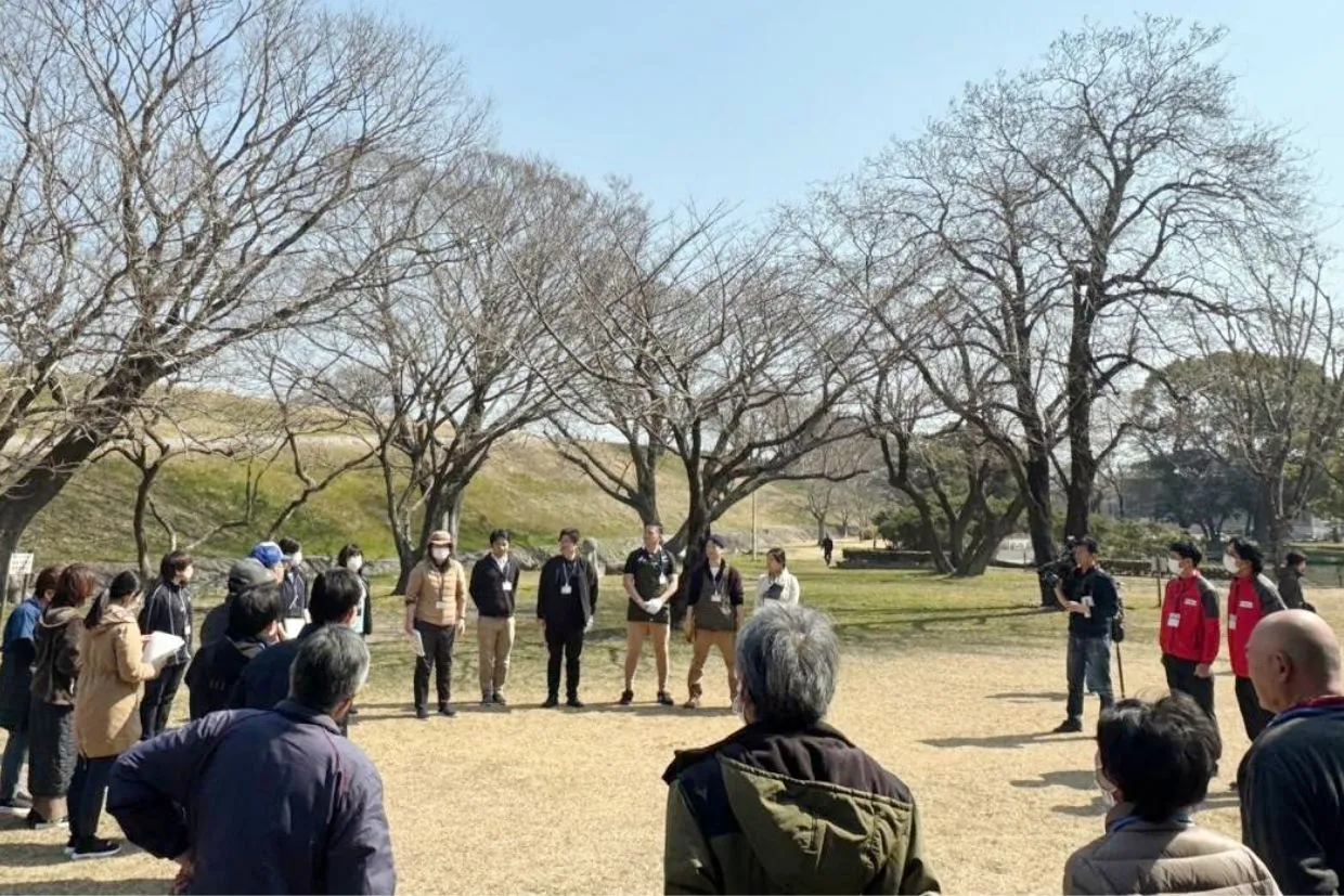 岡崎市、豊橋市の保険代理店、株式会社クワイエットが開催したみんなでつながる実行委員会の様子。公園で、中央に株式会社クワイエットの社員たちが立ち、防災イベントの参加者たちにイベントの内容を説明している。