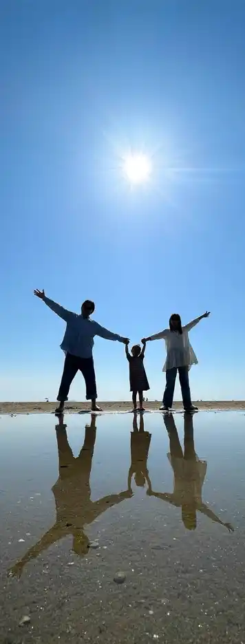 家族3人が手を繋いで芝生の上に立つ後ろ姿。幼い男の子を真ん中に両親が両脇に立っている。