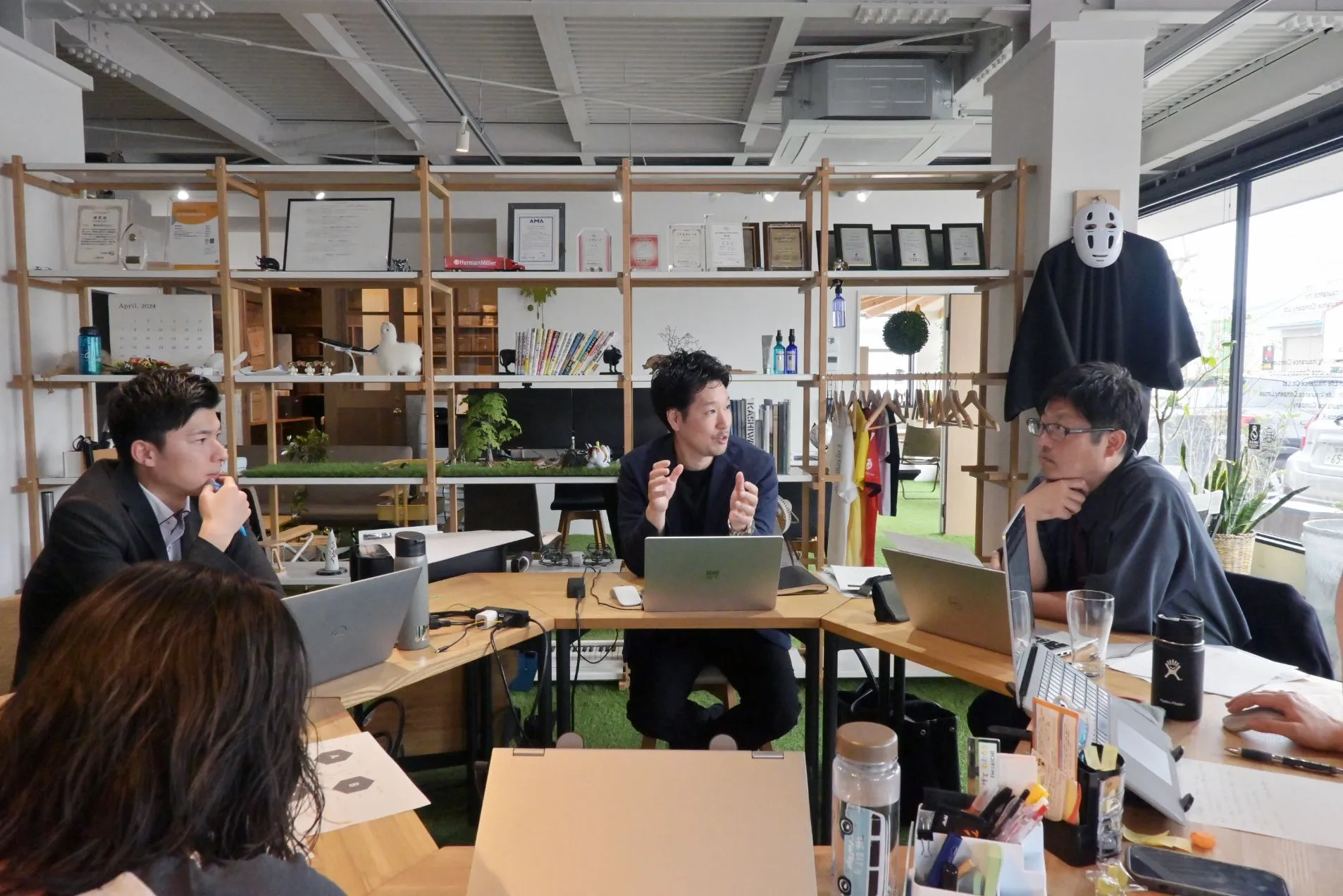 岡崎市、豊橋市の株式会社クワイエットのオフィスで、テーブルを囲んで座り、会議をしている様子。中央の男性社員が右側の男性社員に向かって話していて、他の人が話を聞いている。